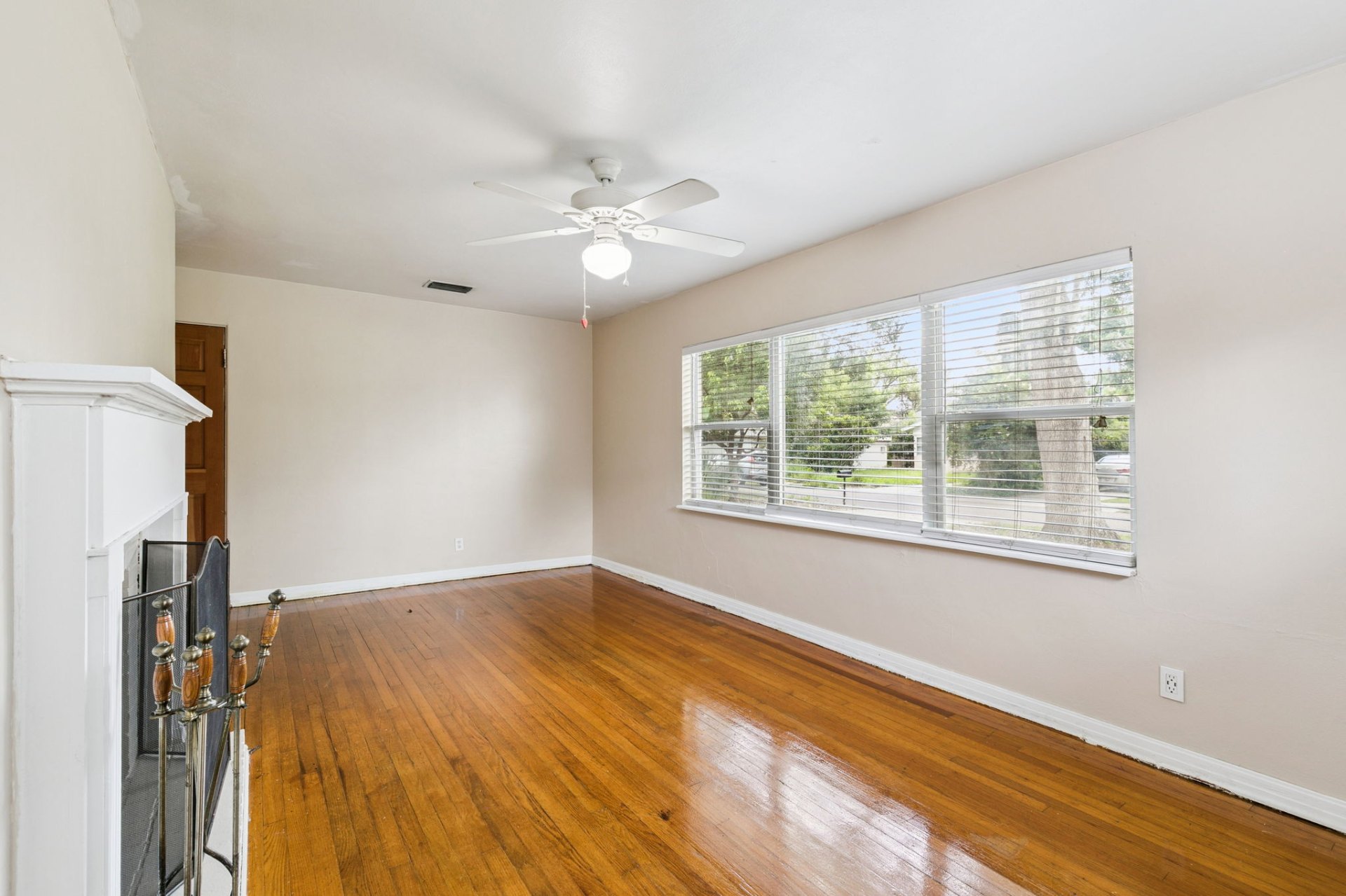 Sunlit living room with refinished hardwood floors, wood-burning fireplace, and a wide picture window