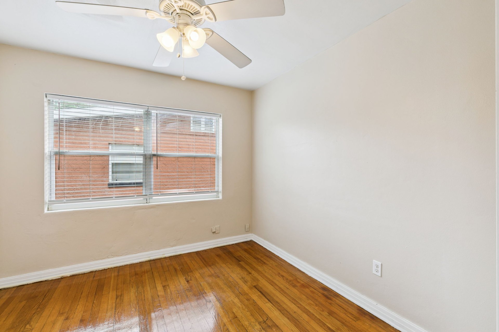 Peaceful bedroom with a large window, ceiling fan, and classic mid-century hardwood flooring