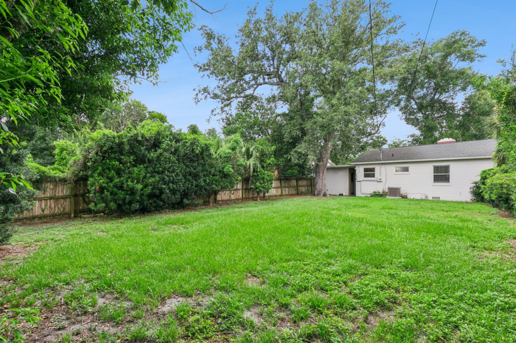 Expansive fully fenced backyard shaded by a mature oak behind the concrete-block cottage