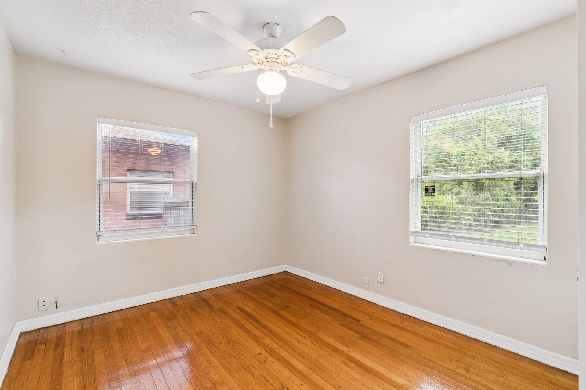 Bright corner bedroom with two windows, ceiling fan, and gleaming original hardwood floors