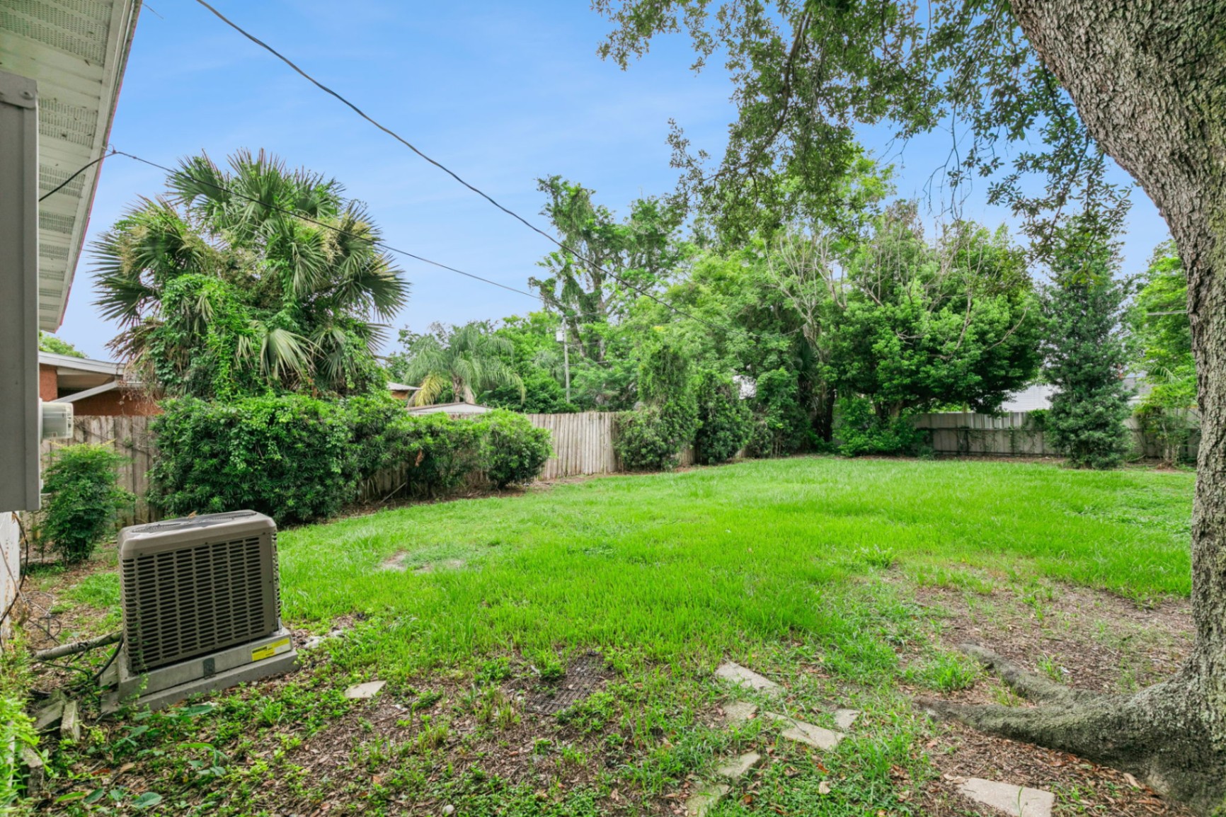 Grassy fenced backyard framed by mature oaks and tropical landscaping with room to play or garden
