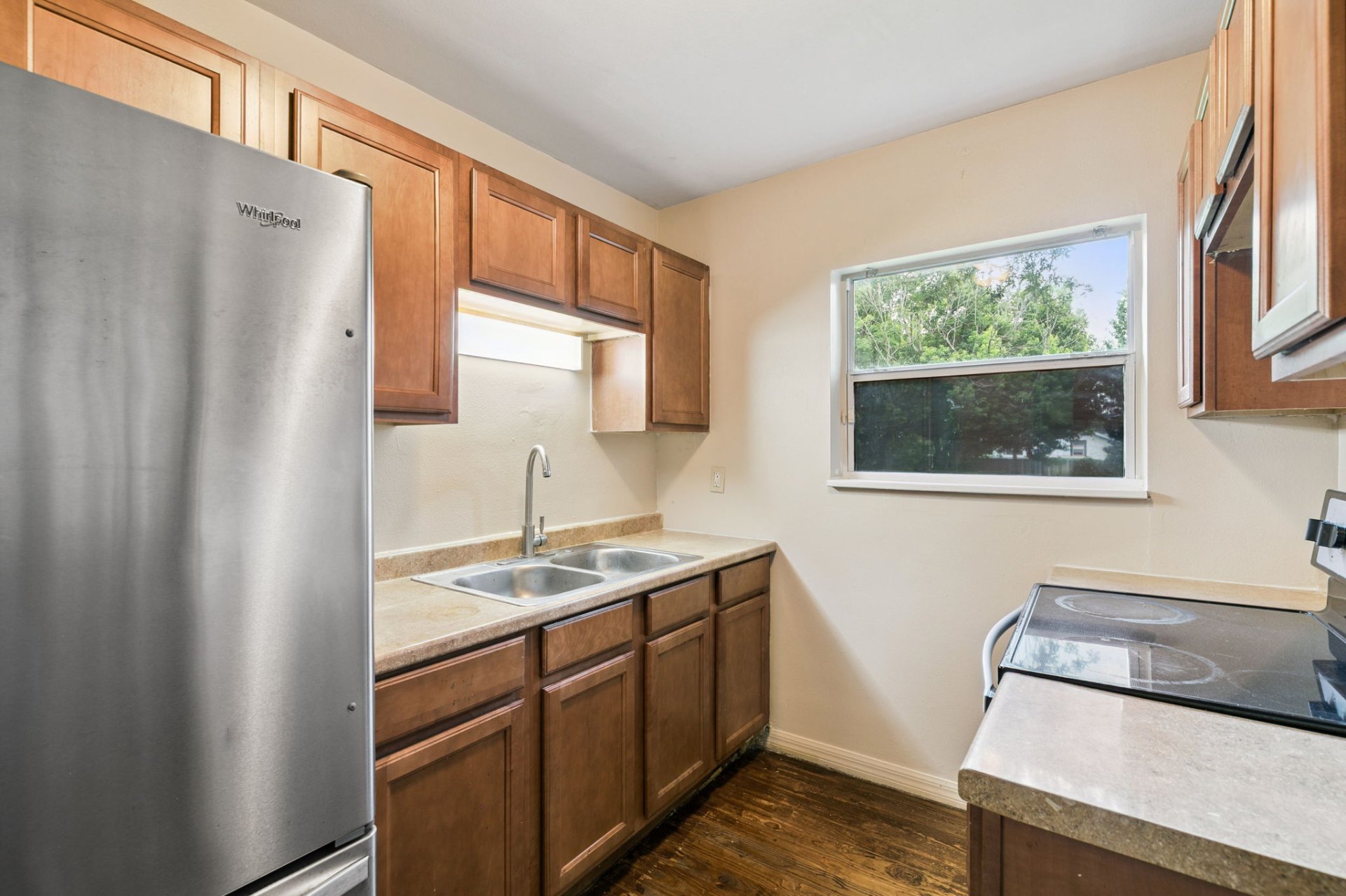 Galley kitchen with stainless refrigerator, warm wood cabinetry, and a sunny backyard-view window