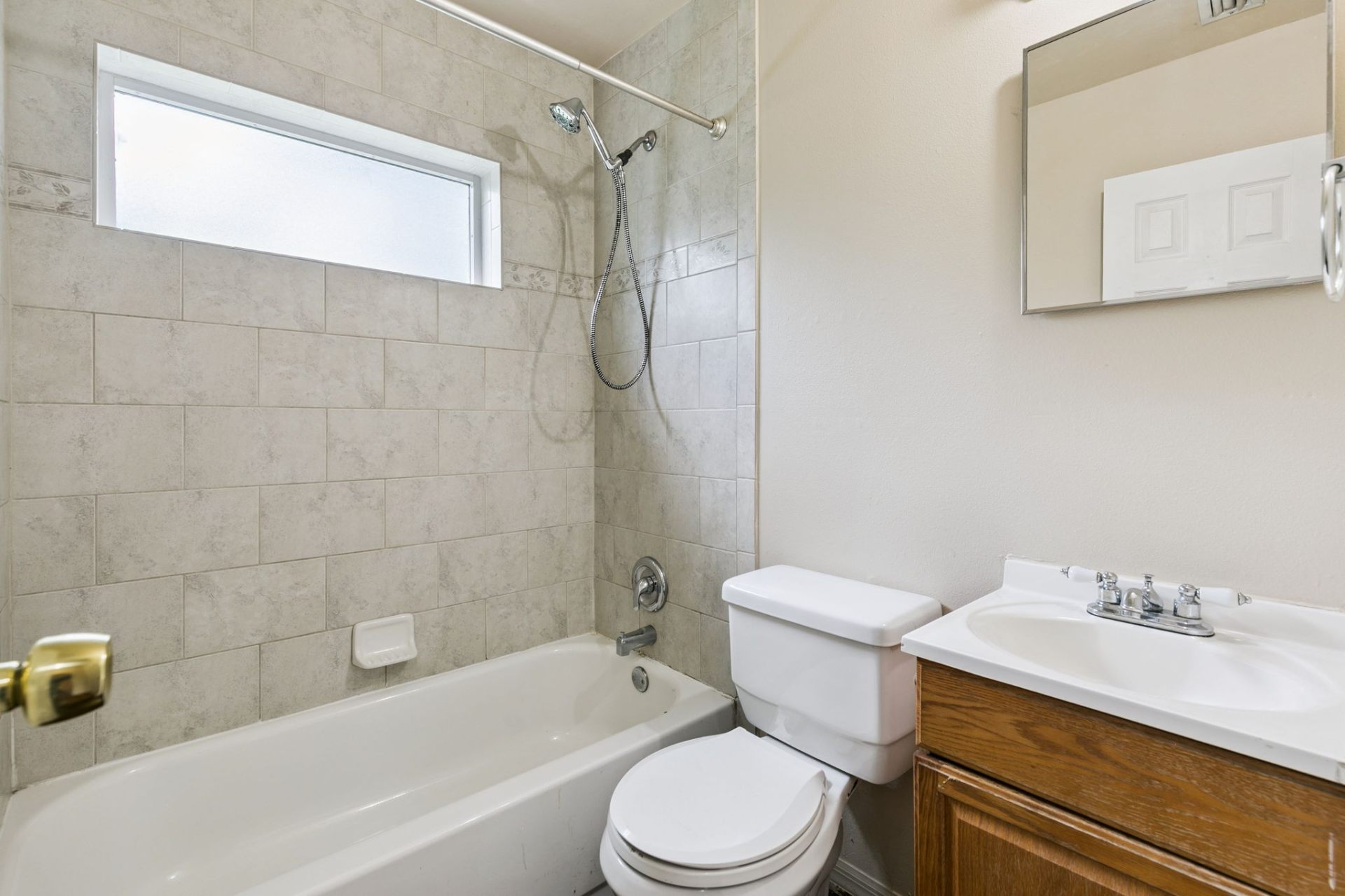 Full bath with tiled tub and shower, privacy glass window, and oak vanity with white countertop