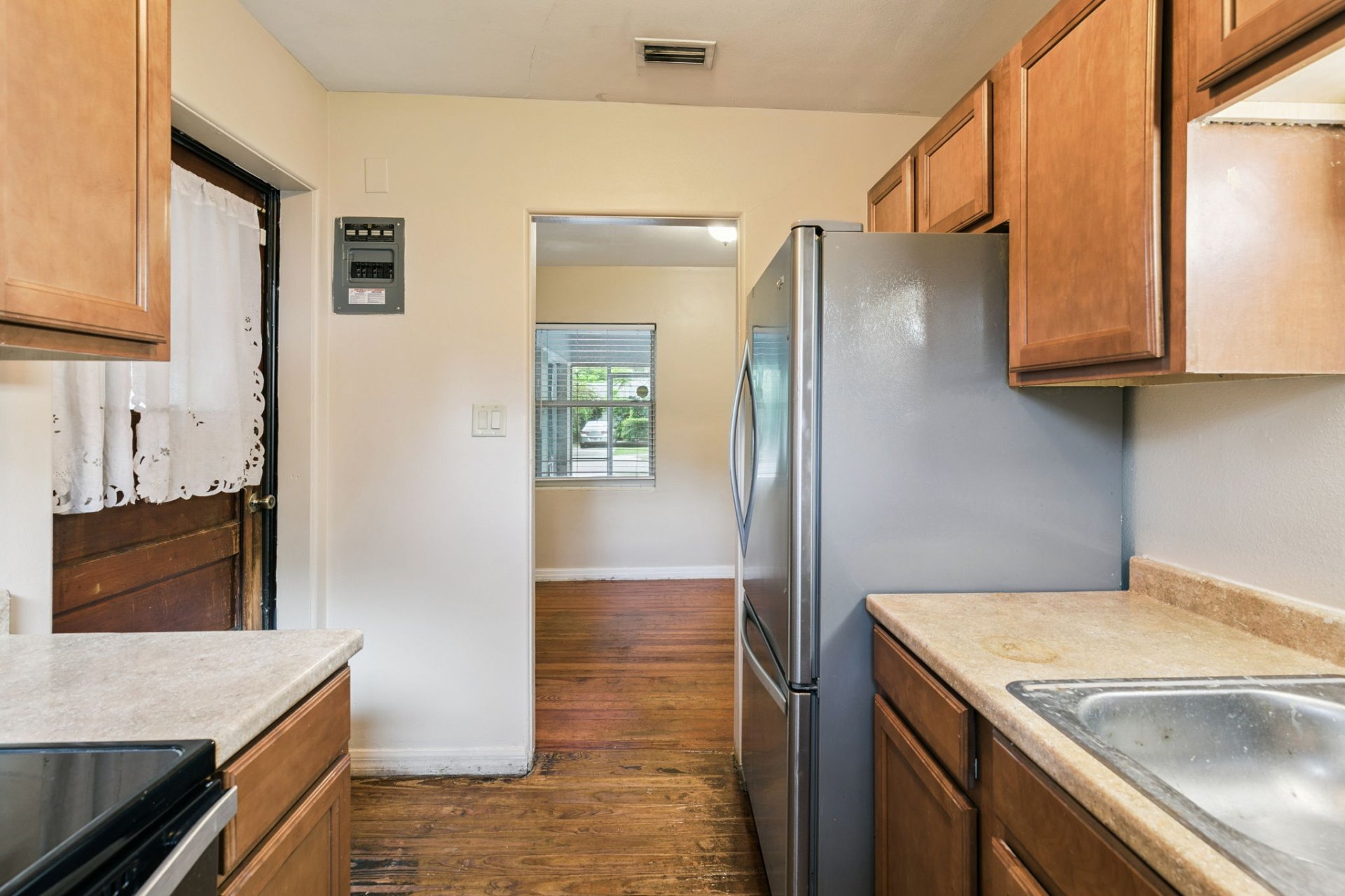 Galley kitchen with back-door access, stainless fridge, and sightline through to the sunny front rooms
