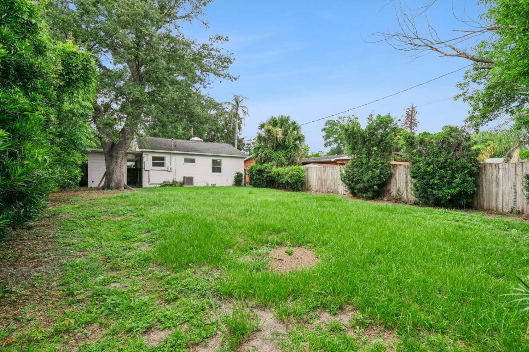 Deep, private backyard with lush lawn, wood privacy fence, and towering mature oaks